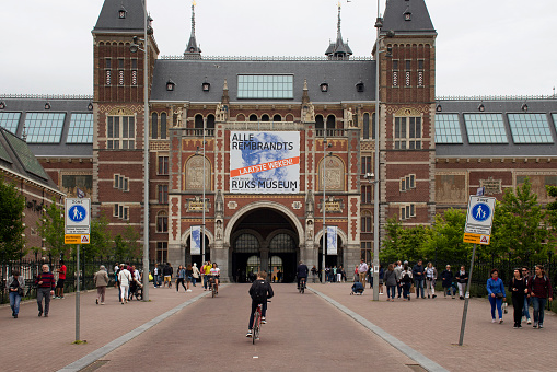 View of people walking and riding bicycles in front of Rijksmuseum. It is a Dutch museum dedicated to arts and history, located at the Museum Square in the borough Amsterdam South.