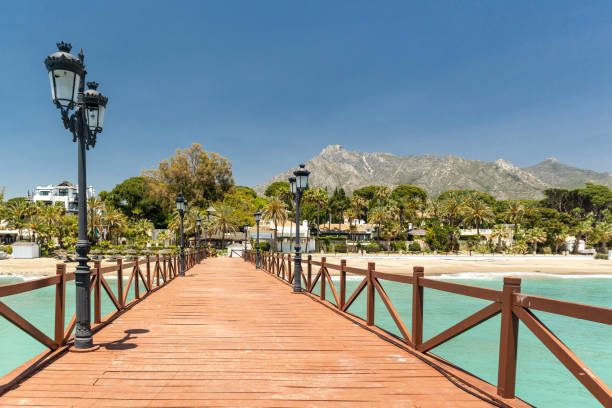 View of red wood bridge "Embarcadero" in Marbella. SPAIN View of red wood bridge "Embarcadero" in Marbella. View of Luxury area Puente Romano, expensive urbanisations. Mountain "La Concha". Spectacular travel destination. Emerald water, no people marbella stock pictures, royalty-free photos & images