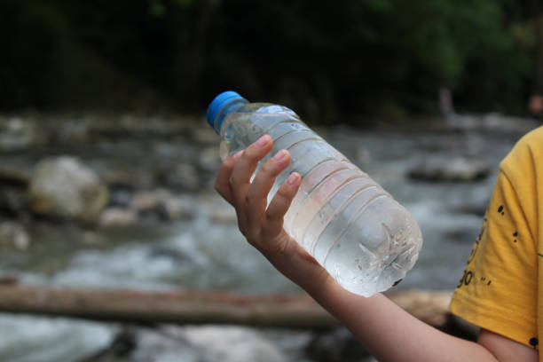 view of stream flowing between trees and a bottle of water stock photo