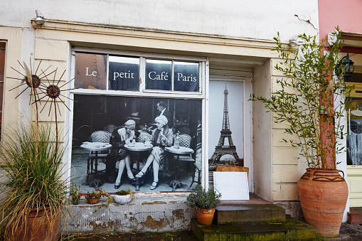 Homburg, Germany - March, 27 - 2016: View of the „Le petit Café Paris“ entrance and window part, equipped with an old image of an old Paris Coffee shop scene, two women sitting at a round table, having fun, talking.
