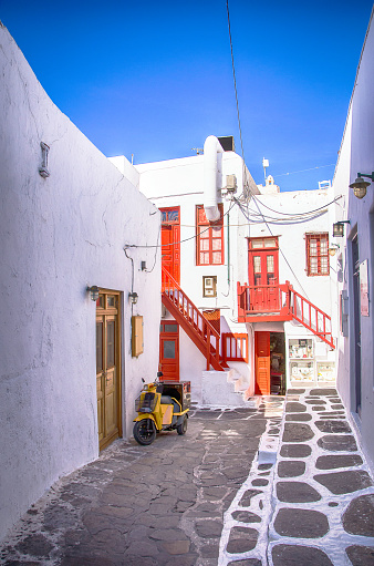 A view of whitewashed street with red doors and windows and cute motorbike in beautiful Mykonos town, Greece