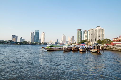View upstream river Chao Phraya from  Asiatique at Chao Praya river in Bangkok. On rver are boats. In background is modern cityscape. Asiatique is promenade area with restaurants in southern Bangkok
