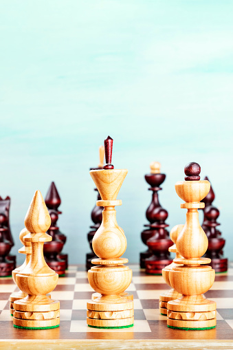 Vintage chess figures on a board at the very beginning of the game, on a teal background with copy space