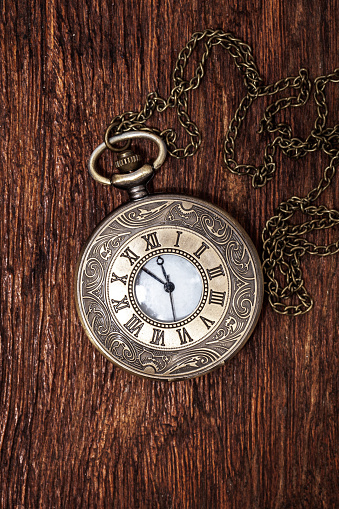 A pocket watch rests on a calendar. The image is captured using a very shallow depth of field and on a light blue background that provides ample room for copy and text.