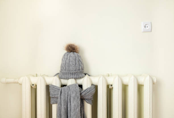 Vintage heating radiator with wool knitted winter hat and scarf. The electricity and gas bill goes up, European energy crisis concept. Background copy space, room for text. stock photo