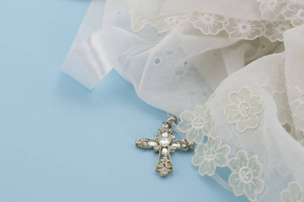 Vintage lace christening gown with Christian cross pendant isolated on light blue background stock photo