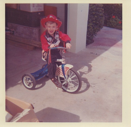 Vintage Photograph of a young boy in a cowboy outfit sitting on a tricycle. Circa 1965.