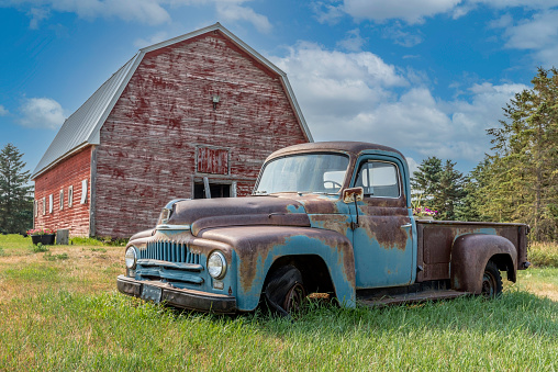 Vintage red barn with abandoned pickup truck on the prairies in Saskatchewan