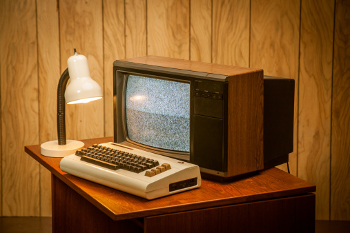 Product photo of an old commodore vic-20 vintage retro computer on wood desk, an 80's lamp and wood panelling in the back.