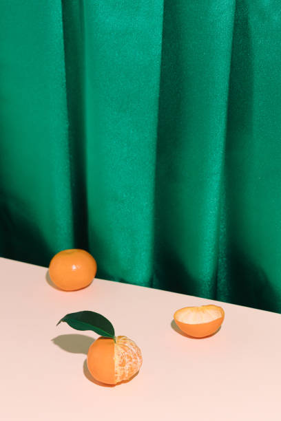 Vintage style concept with green curtain and peeled and unpeeled tangerine fruit. stock photo