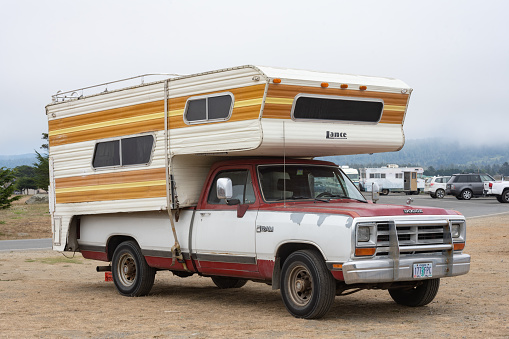 In Crescent City, USA a vintage Dodge Ram truck with an old fashioned camper top and Oregon plates is parked at the beach on a foggy summer day.