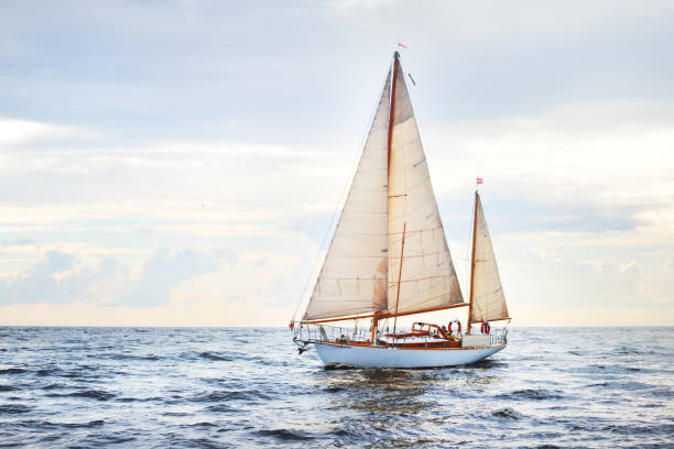 Vintage wooden two mast yacht (yawl) sailing in a open sea on a clear day. Waves and white clouds stock photo