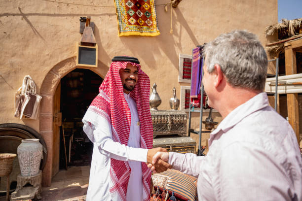 Visiting businessman connecting with Middle Eastern merchant Mature global traveller in western attire shaking hands with young local salesman as he explores the town and its commercial opportunities. agal stock pictures, royalty-free photos & images