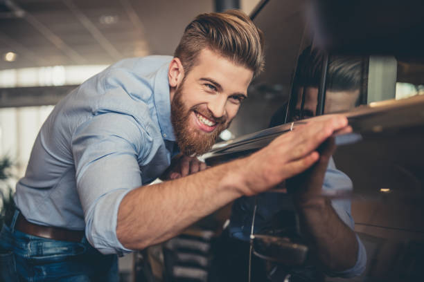 Visiting car dealership Visiting car dealership. Handsome bearded man is stroking his new car and smiling man driving suit stock pictures, royalty-free photos & images