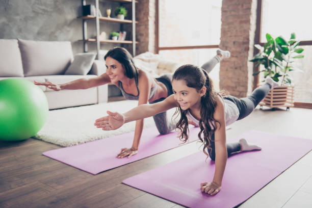 Vitality concept. Watch repeat the moves, poses from the helpful video! Cute sweet cheerful joyful with long hair schoolgirl and slim sportive mom are doing stretching exercises in room om purple mats  relaxation exercise stock pictures, royalty-free photos & images