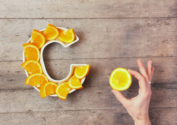 vitamin c or ascorbic acid nutrient in food concept. plate in shape of letter c with orange slices and woman's hand with citrus making sign ok on wooden background. flat lay or top view. - alimentos sistema imunitário imagens e fotografias de stock