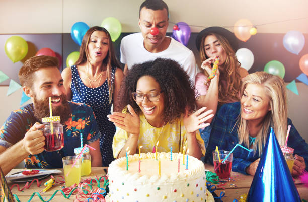Vivacious woman blowing out her birthday candles Vivacious attractive young African woman with an afro hairstyle sitting at a table with her friends celebrating and blowing out her birthday candles happy birthday in danish stock pictures, royalty-free photos & images