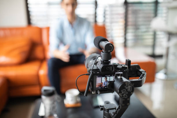 Vlogging at home Young handsome man sitting at home on sofa and recording a video with professional camera, looking at camera and talking, focus on foreground filming stock pictures, royalty-free photos & images