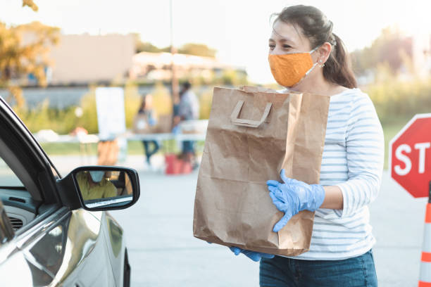 Volunteer gives out food during food drive A female volunteer prepares to bag of food to someone in a car during a drive through food drive. food bank stock pictures, royalty-free photos & images