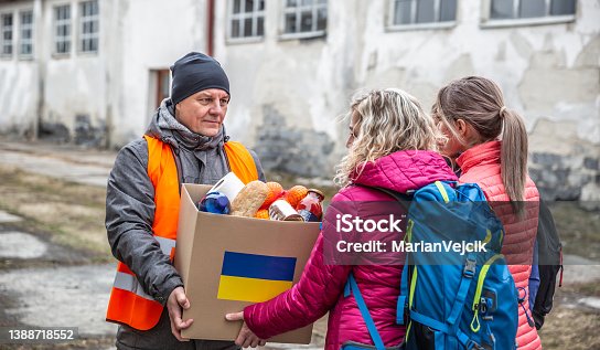 istock Volunteer in orange west gives a box of food donation to fleeing refugees from Ukraine. 1388718552
