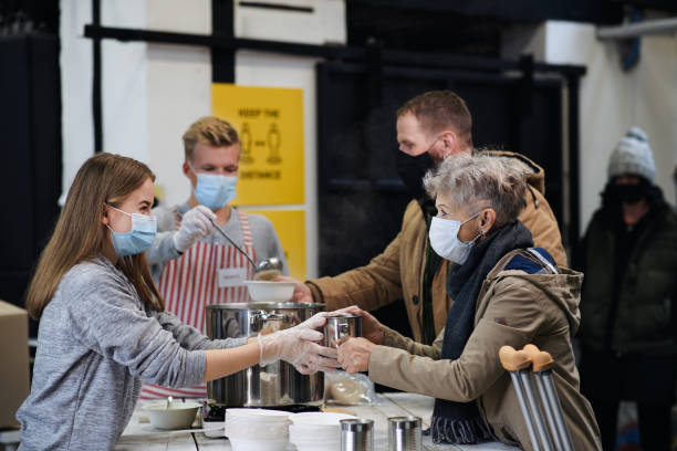 Volunteers serving hot soup for homeless in community charity donation center, coronavirus concept. Volunteers serving hot soup for ill and homeless in community charity donation center, food bank and coronavirus concept. homelessness stock pictures, royalty-free photos & images