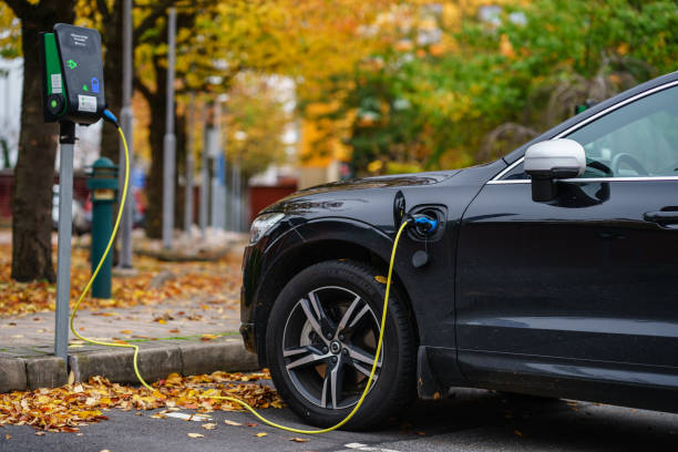 volvo car is plugged in for charging on street parking lot with beautiful autumn view background - electric car imagens e fotografias de stock