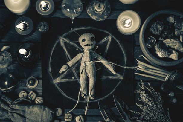 Voodoo Magic concept. Voodoo doll studded with needles with pierced rag heart on pentagram and around burning candles. Spooky or eerie magical esoteric ritual, black and white photo stock photo