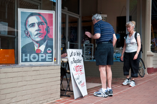 Charlottesville, Virginia, USA - June 7, 2012: An image of Barack Obama sits in a window beside two people, a man and woman, who are talking to a person registering voters. The sign says \