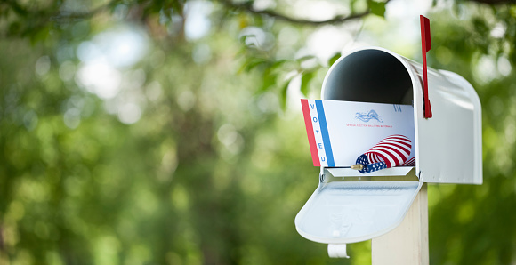 Voting by mail concept. Absentee ballot envelope in a mailbox against a defocused nature background.