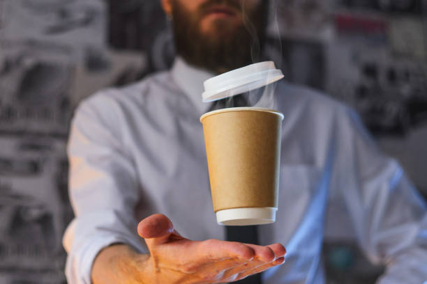 A waiter and a hovering cup of hot coffee Levitating in the air paper cup with hot coffee. Barista, a bearded young man in a white shirt with a tie, creates miracles - advertises his drink, causing it to soar. Logoplacement concept bar drink establishment photos stock pictures, royalty-free photos & images