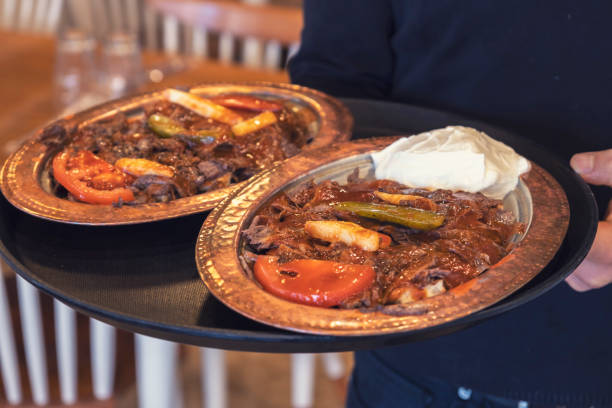 Waiter holding Iskender Kebab plates with food serving guests in a restaurant. stock photo