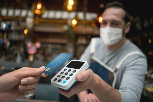 Waiter wearing a facemask while getting a contactless payment at a restaurant Waiter wearing a facemask while getting a contactless payment at a restaurant â COVID-19 lifestyle concepts. **DESIGN ON CREDIT CARD WAS MADE FROM SCRATCH BY US** credit card purchase stock pictures, royalty-free photos & images