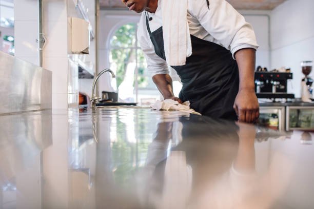Waiter wiping the counter top in the kitchen Cropped shot of waiter wiping the counter top in the kitchen with cloth. Man cleaning and maintaining commercial kitchen hygiene. Cleaning a Restaurant Kitchen stock pictures, royalty-free photos & images
