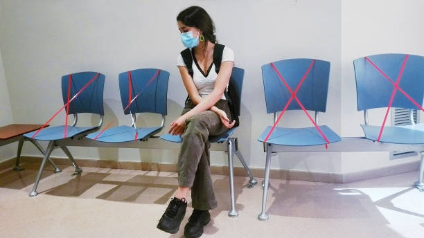 Waiting room, security rules. Young girl sitting, waiting with arms crossed, wearing protective face mask, in coronavirus time stock photo