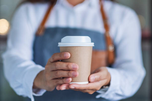 A waitress holding and serving a paper cup of hot coffee A waitress holding and serving a paper cup of hot coffee in cafe barista stock pictures, royalty-free photos & images