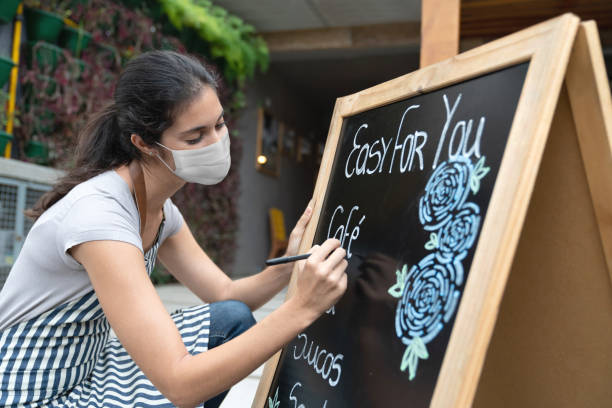 Waitress wearing a facemask while writing the menu at a restaurant Waitress wearing a facemask while writing the menu at a restaurant on a board during the COVID-19 pandemic â reopening of business concepts menu board structure stock pictures, royalty-free photos & images