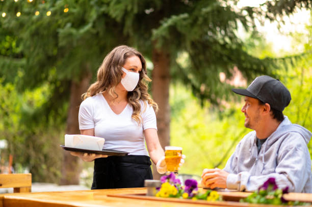 Waitress wearing protective equipment for COVID Server wearing a face mask to prevent the spread of COVID-19 dining stock pictures, royalty-free photos & images