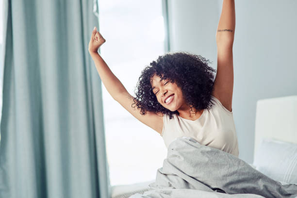 Wake up, there's life to be lived! Shot of a happy young woman sitting on the bed in the morning and stretching waking up stock pictures, royalty-free photos & images