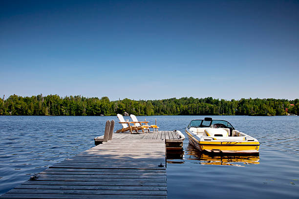 Wakeboard boat and Dock Two Adirondack chairs on Sunny Dock with Wakeboard boat. Horizontal. motorboat stock pictures, royalty-free photos & images