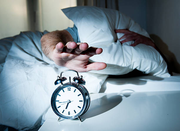 Waken man stretching hand to turn off alarm clock stock photo