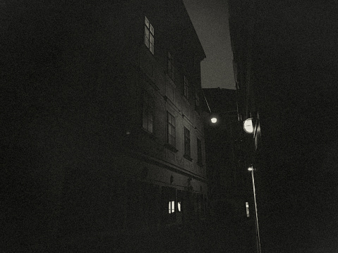 A dark and narrow alley in Vienna. It is night and only a sparse street lighting gives some light in the darkness.