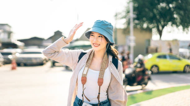 Walking young adult southeast asian woman traveller wear blue hat and backpack under sunlight stock photo
