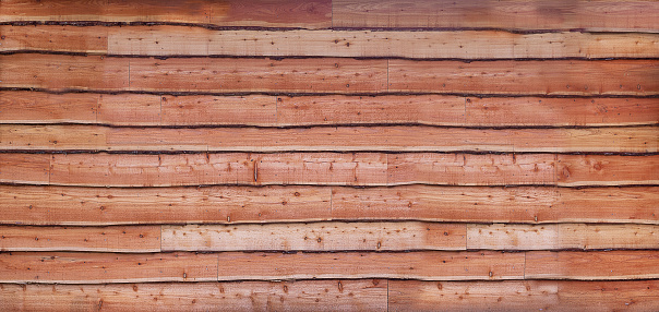 Flat view of wall of rustic waney uneven edge wooden cladding boards