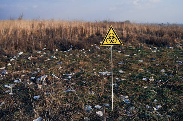 Warning biohazard sign in field with garbage. Yellow triangle with biohazard symbol warning on abandoned territory with trash. Garbage waste field with biological hazard sign. Concept of ecology, environmental pollution and danger. contamination stock pictures, royalty-free photos & images