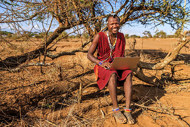 Warrior from Maasai tribe using laptop, Kenya, Africa African warrior from Maasai tribe using laptop, central Kenya, Africa. Maasai tribe inhabiting southern Kenya and northern Tanzania, and they are related to the Samburu. maasai warrior stock pictures, royalty-free photos & images
