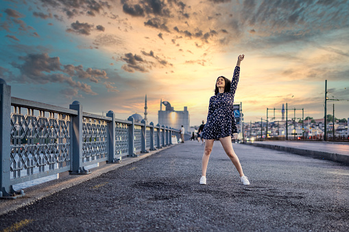 Girl standing on the bridge at sunset, raising her hand