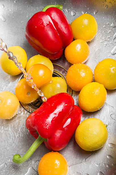 Washing red and yellow fruits and vegetables in the kitchen sink.