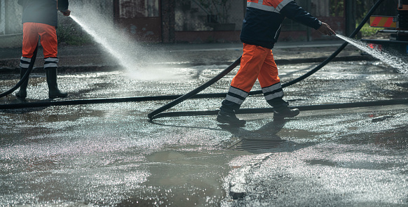 Worker cleaning driveway with  high pressure washer splashing the dirt on asphalt