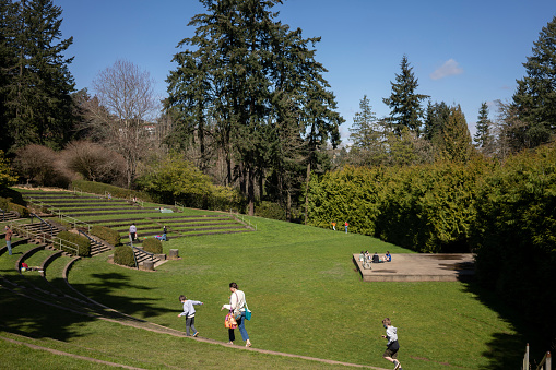 Portland, OR, USA - Mar 23, 2021: A mother walks along the steps with her kids in the Washington Park amphitheater in Portland, Oregon. Visitors to the public urban park enjoy the outdoors on a sunny day as springtime comes amid the coronavirus pandemic.