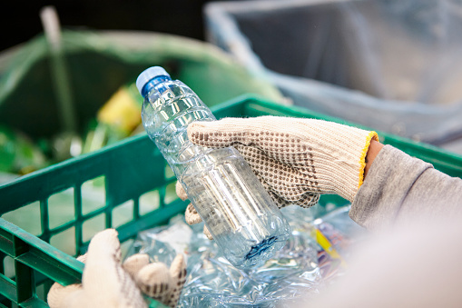 High angle view of waste management worker using work gloves holding plastic bottle in recycling plant